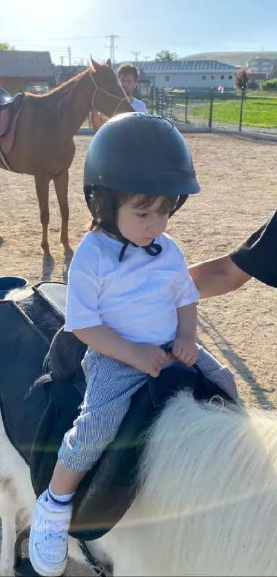 Young child riding a pony on a sunny day outdoors, wearing a safety helmet.