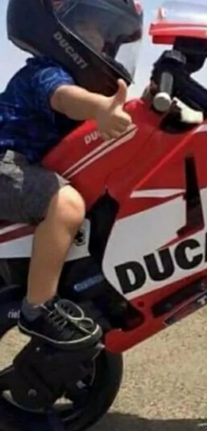 Child rides a red Ducati toy motorcycle under a clear sky.