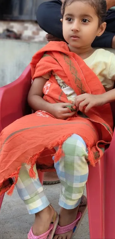 Child sitting in a red chair draped with orange cloth.