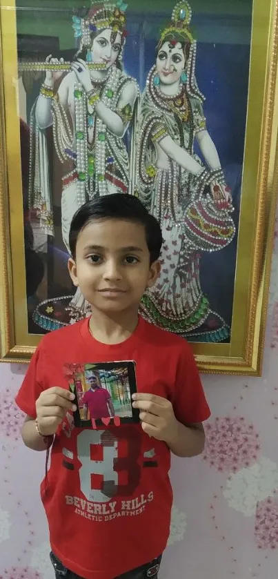 Young child holding a photo in front of framed artwork.