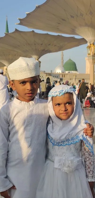 Children in traditional attire at a mosque with large parasols.