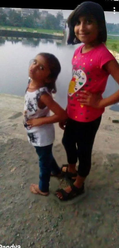 Two children happily pose by a scenic lakeside view.