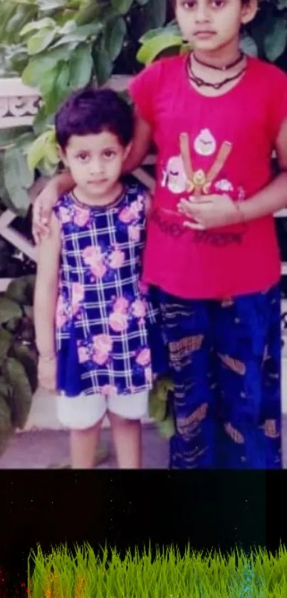 Two children standing in a garden with lush greenery.