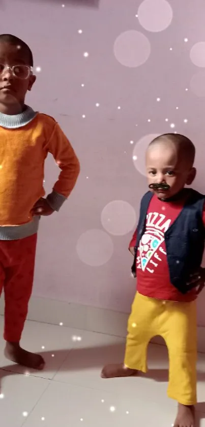 Two children pose in colorful outfits on a light pink background.