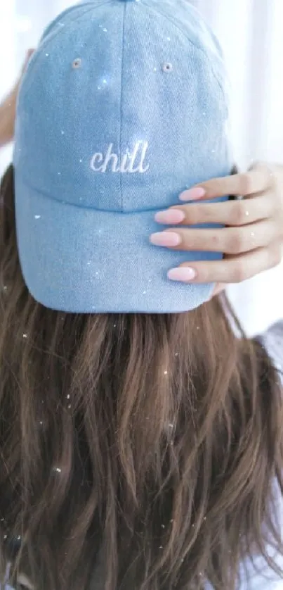 Woman with long hair wearing a denim cap labeled 'chill' from behind.