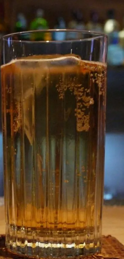 A chilled drink in a tall glass with ice and bubbles on a bar counter.