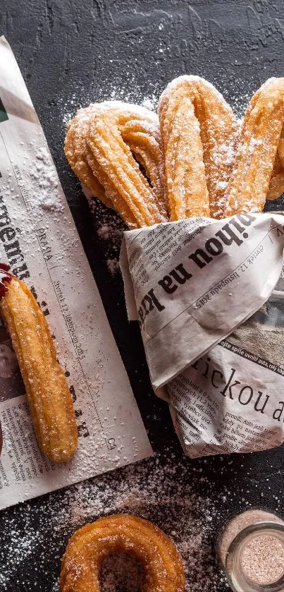 Churros wrapped in newspaper with chocolate dip on dark background.