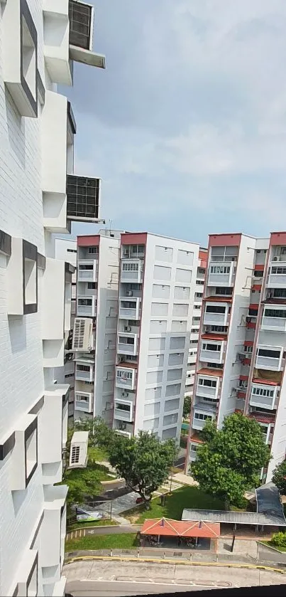 City apartment view with white buildings and greenery under a blue sky.