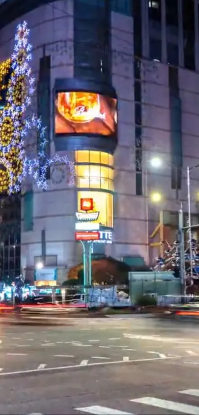 Vibrant city street at night with Christmas lights and a towering festive display.