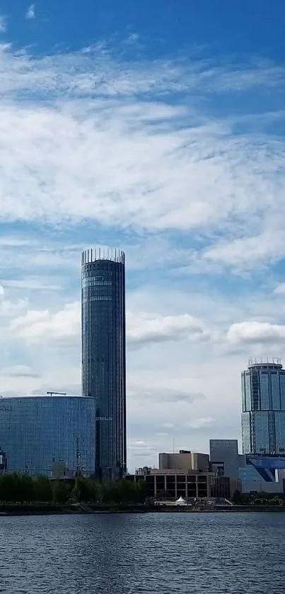 City skyline with tall buildings under a clear blue sky reflected in water.