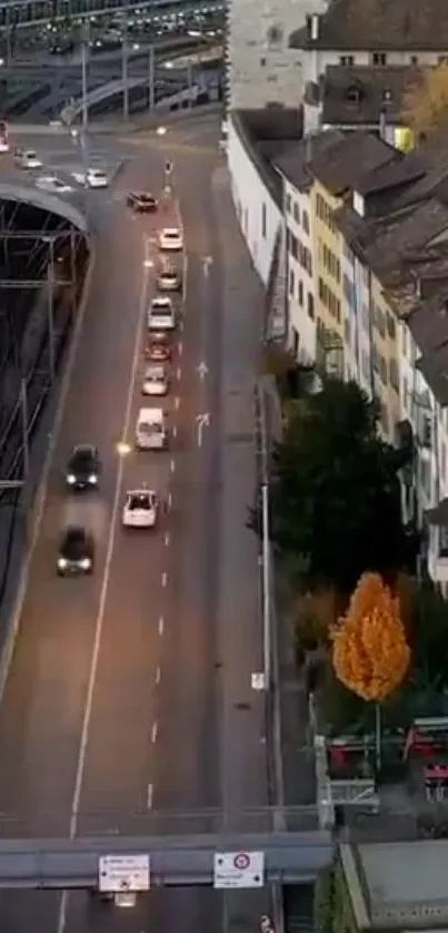 Aerial view of city street at dusk, lined with cars and vibrant buildings.