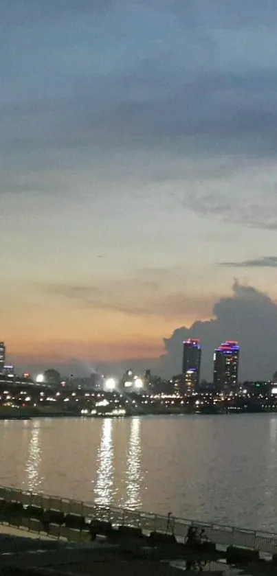 City skyline at dusk with glowing lights and river reflection.