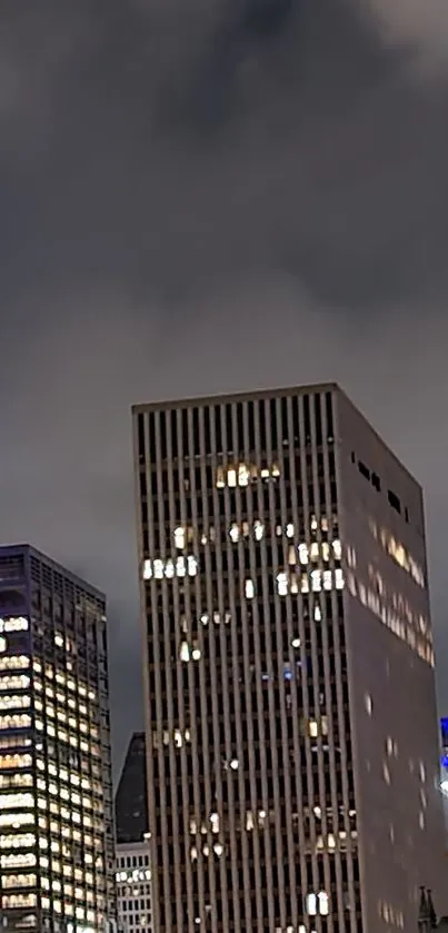 Nighttime cityscape with tall, illuminated skyscrapers under a cloudy sky.