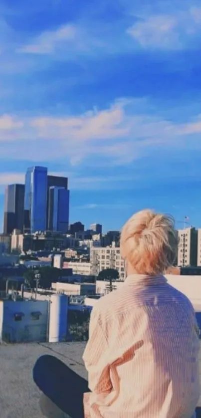 Person sitting on a rooftop with blue sky and cityscape in the background.