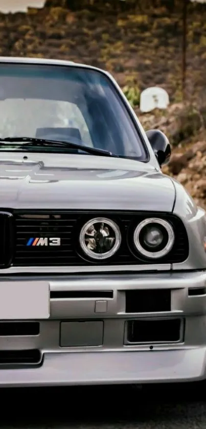 Front view of classic BMW M3 on a scenic road with mountains.