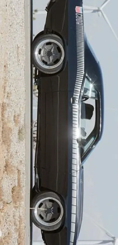 Classic black car in desert setting with wind turbines in the background.