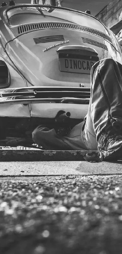 Monochrome image of a mechanic under a vintage car in a garage workshop.