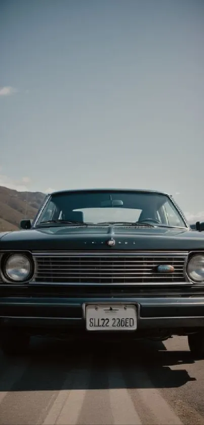 Front view of a classic black car on a scenic road with a mountain backdrop.