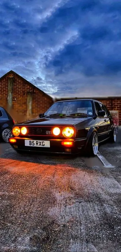 Classic car with glowing headlights under a dramatic evening sky.