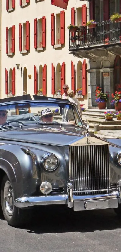 Vintage convertible driving past red-accented buildings.