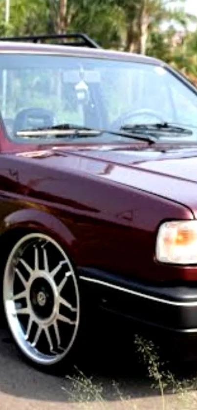 Classic maroon car with sleek wheels, parked roadside.