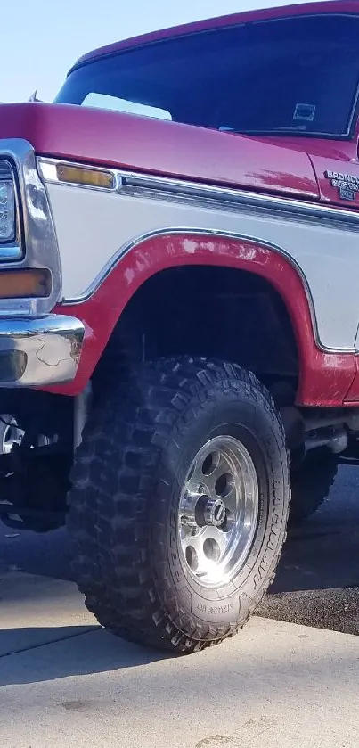 Close-up of a classic red and white off-road truck with rugged tires.