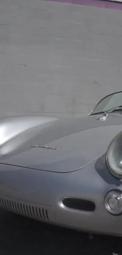 Classic silver car against a concrete wall, showcasing retro design elegance.