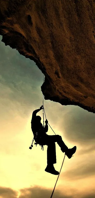 Climber silhouette against golden sunset on rocky cliff.