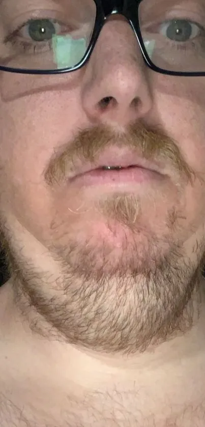 Close-up portrait of a man's face with glasses and facial hair.