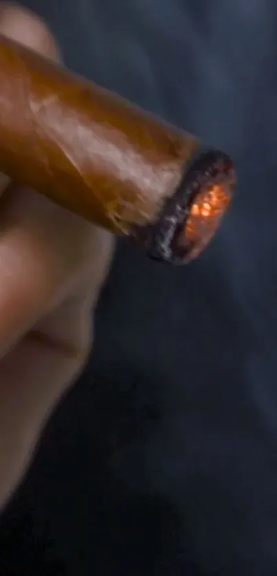 Close-up of a lit cigar with glowing ember, held in hand.