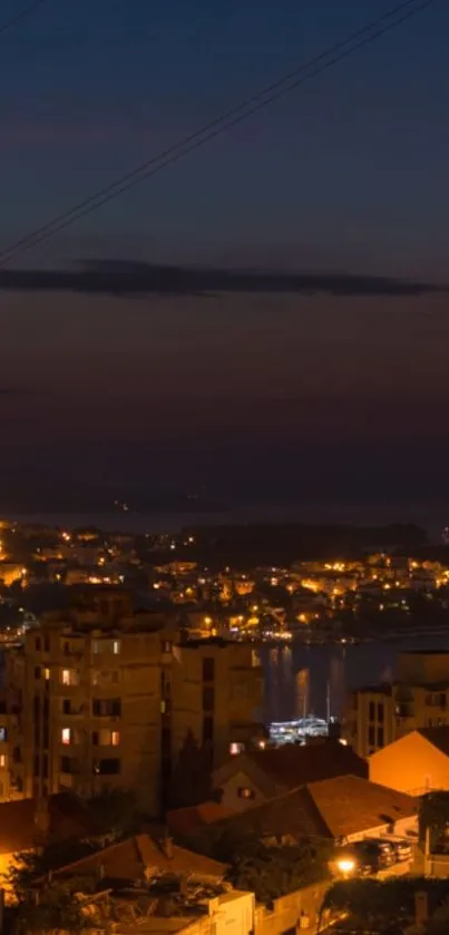 Night view of a coastal city with illuminated buildings and a dark sky.