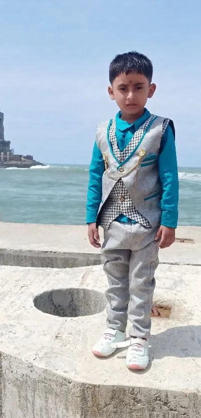 Young boy in turquoise by the sea with a distant statue.