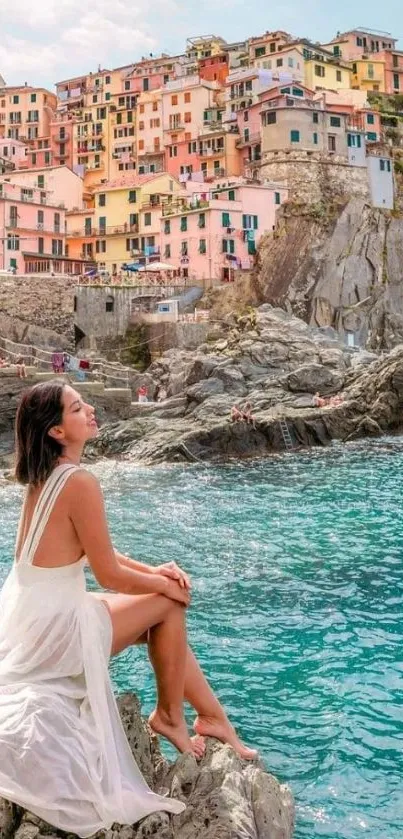 Woman sitting on rocks by a colorful seaside village.