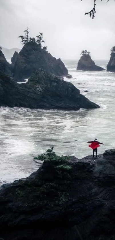 Person with red umbrella on rocky coast with ocean waves.