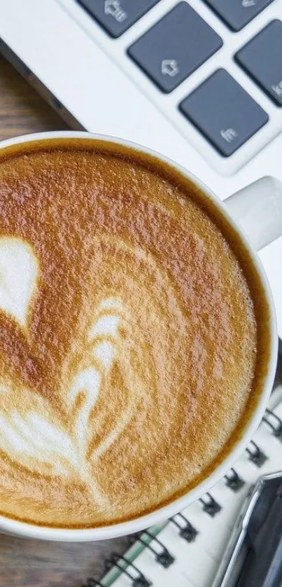 A coffee cup with latte art beside a laptop on a desk.