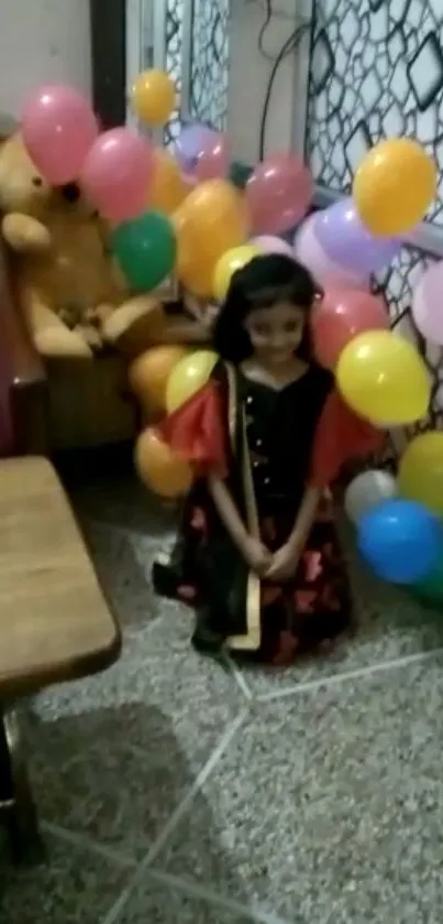 Child smiling surrounded by colorful balloons and a teddy bear.