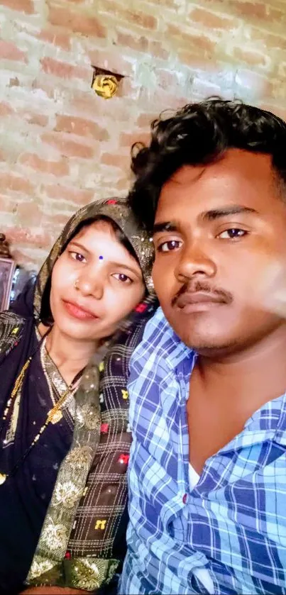 Couple posing in front of a rustic brown brick wall.