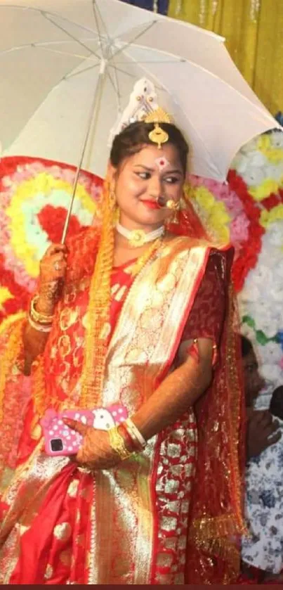 Indian bride in vibrant red attire holding an umbrella, surrounded by festive decor.