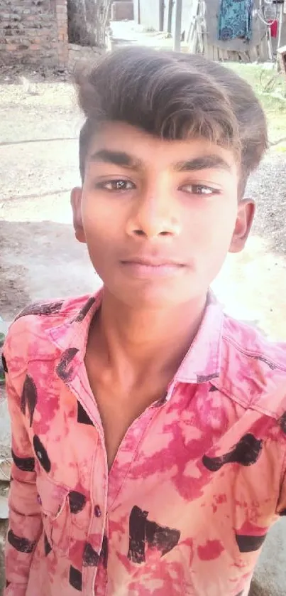 Young man in pink shirt with village background.