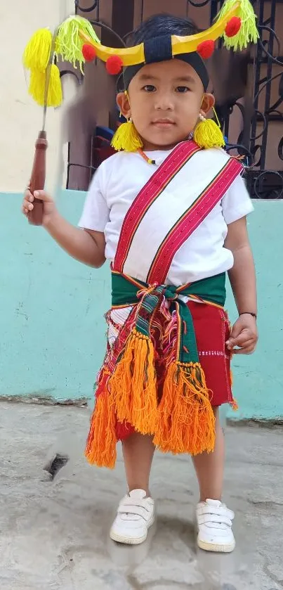 Child in traditional attire with colorful tassels, standing on stone pavement.