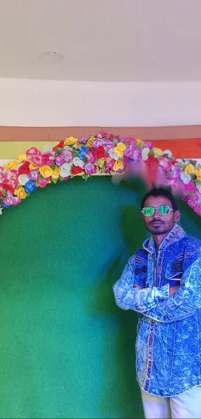 Man in denim with colorful floral arch and green background.