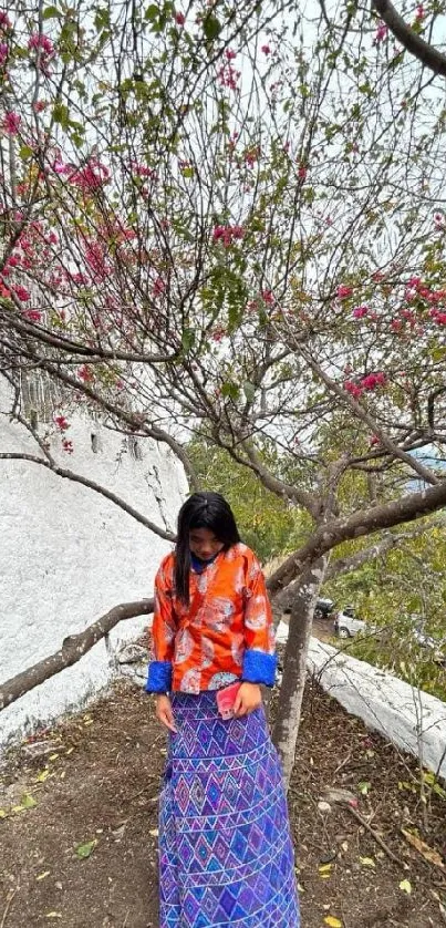 Woman in colorful attire under a flowering tree.