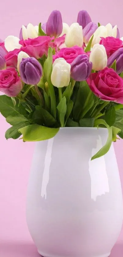 A bouquet of tulips and roses in a white vase on a pink background.