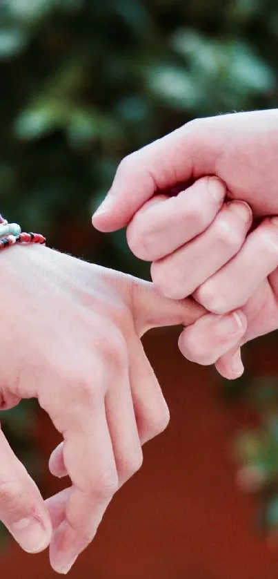 Two hands with colorful bracelets linked by pinkie fingers in front of greenery.