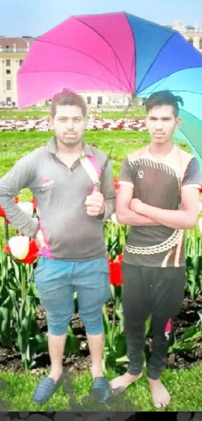 Two men pose with a colorful umbrella in a garden of tulips.