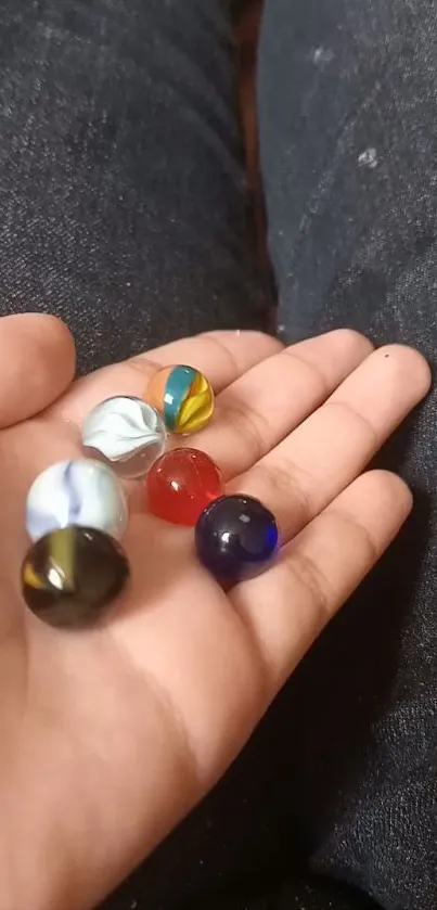 Colorful glass marbles in a hand with a dark fabric background.