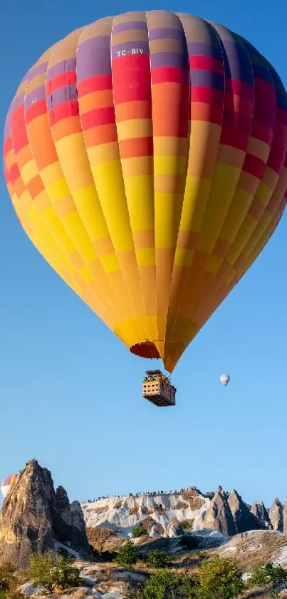 Colorful hot air balloon soaring in clear blue sky over rocky landscape.