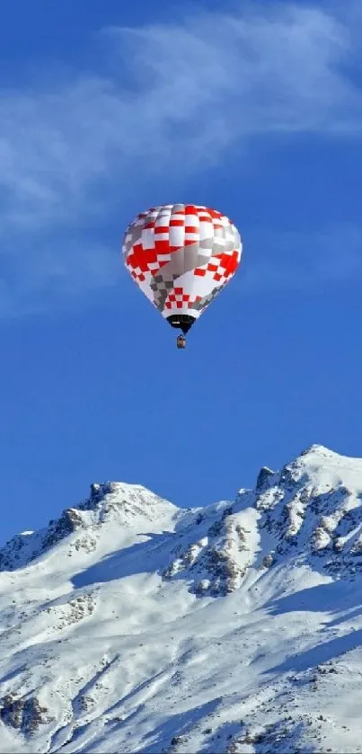 Hot air balloon over snowy mountains under a blue sky.