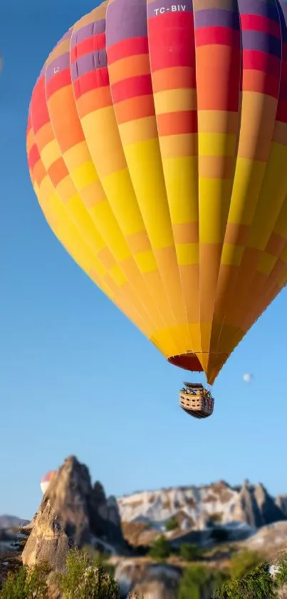 Vibrant hot air balloon soaring over scenic rock formations with a blue sky.