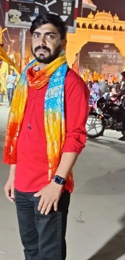 Man in red shirt at Indian festival with colorful scarf and night scene.